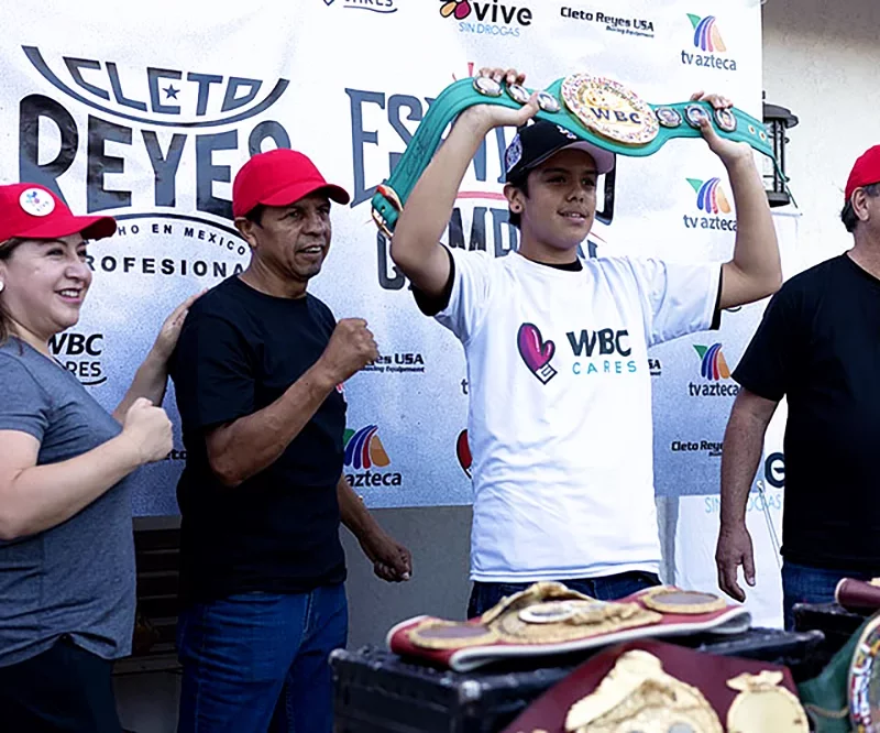 Elizabeth Reyes (WBC Cares collaborator), and members of Cleto Reyes posing with one of the attendees at the 'Espíritu de Campeón', holding a WBC champion belt replica