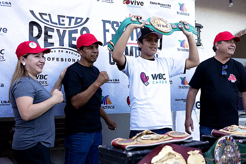 Elizabeth Reyes (WBC Cares collaborator), and members of Cleto Reyes posing with one of the attendees at the 'Espíritu de Campeón', holding a WBC champion belt replica