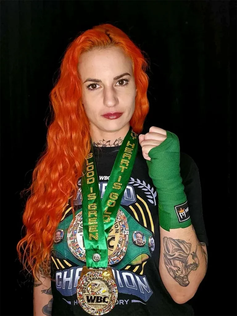 Katia Bissonnette with her fist up posing for the camera with her WBC t-shirt and medal.